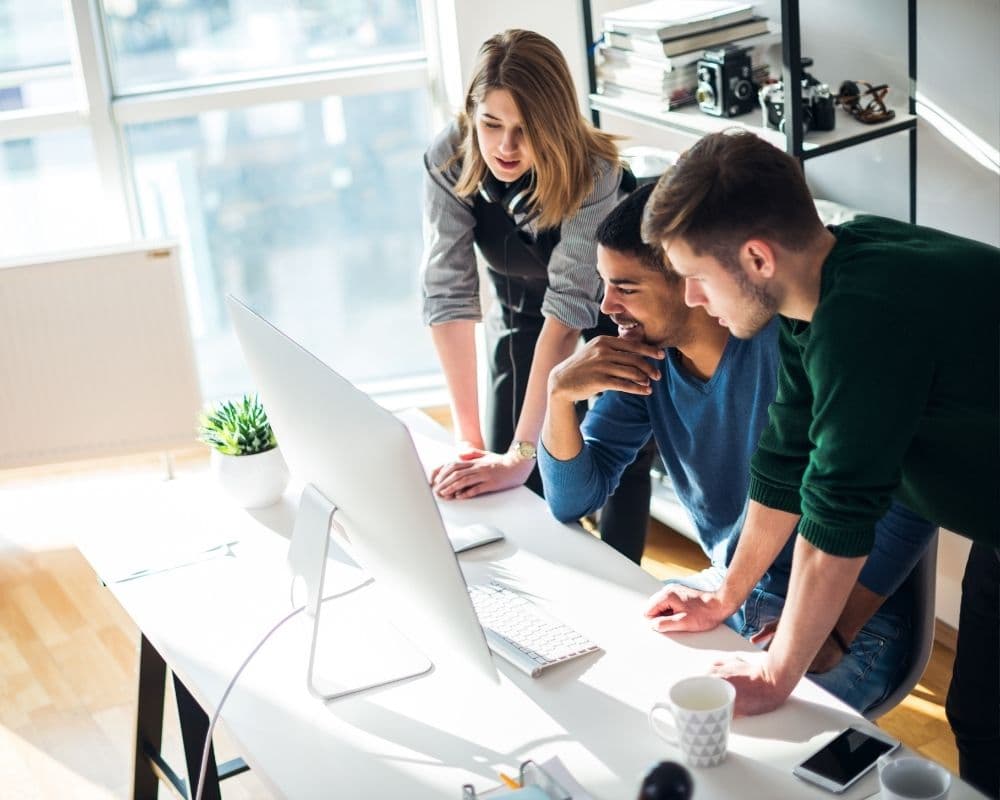 Tres personas trabajando juntas frente a un computador en una oficina luminosa